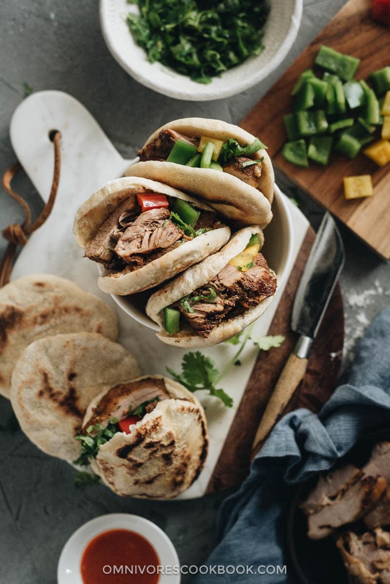 Flatlay of pork belly buns with chopped cilantro and Sriracha sauce